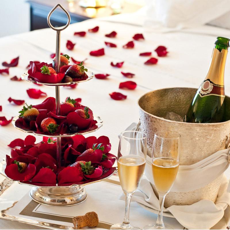 Rosenblätter und Champagner auf gemütlichem Bett